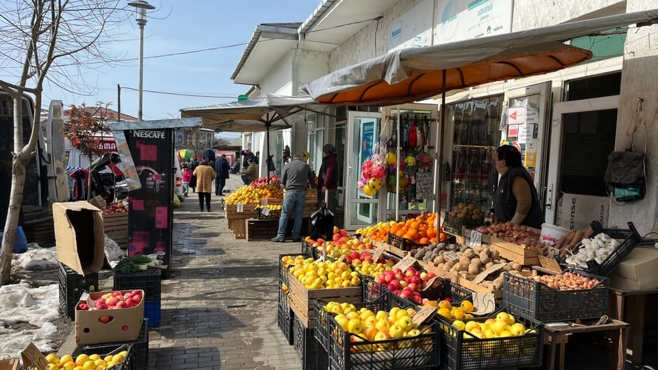 Fruit stand with lots of yellow and red apples in black boxes.  Behind is a woman.