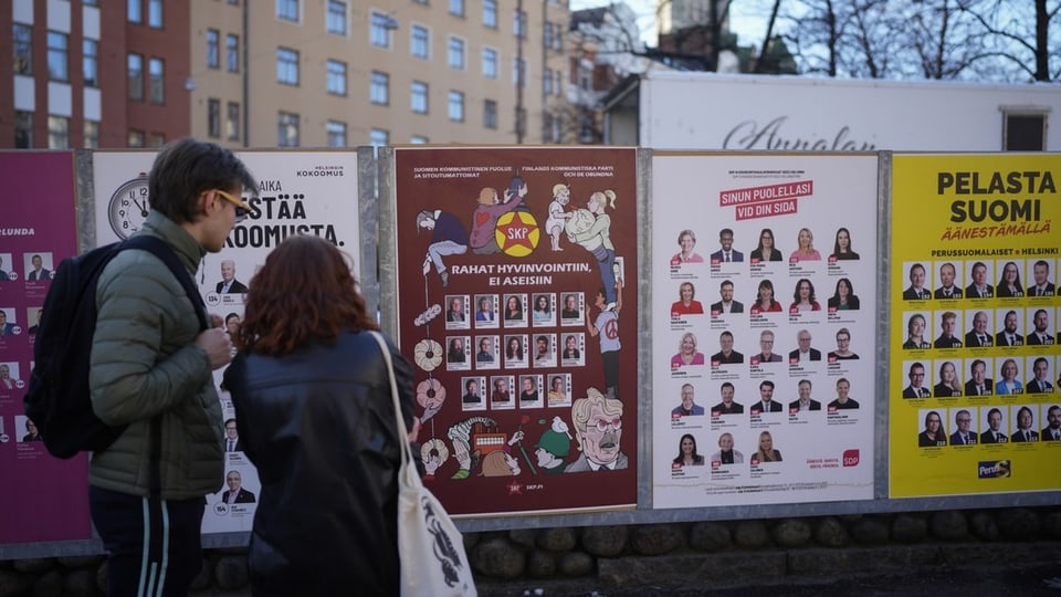 Two people stand in front of Finnish election posters