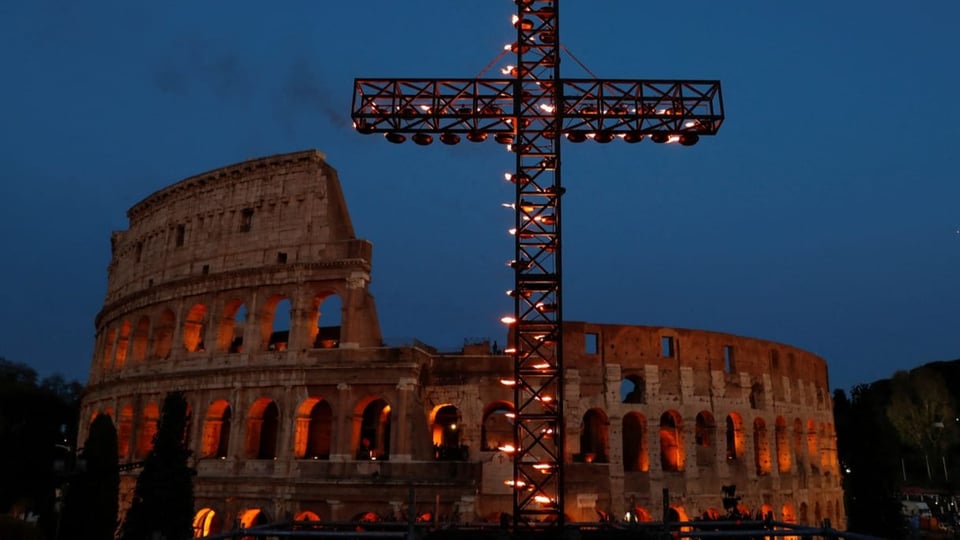 Long shot of the Colosseum in Rome with a cross in the foreground.