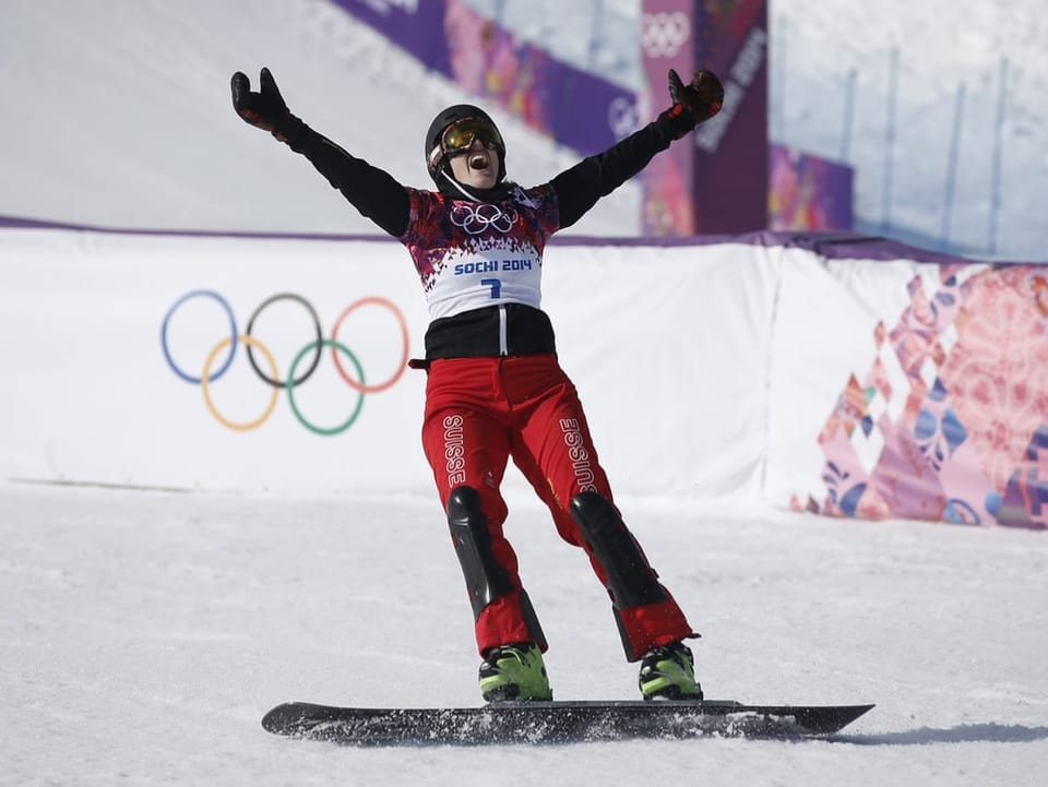 Patrizia Kummer with snowboard on the slope, raises her hands in joy.