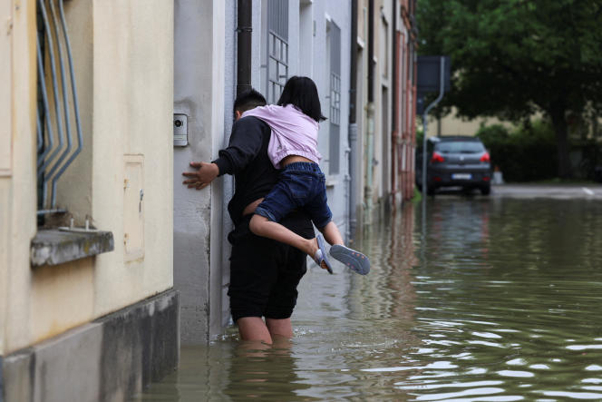A man carries a child on his back as he wades through the waters after heavy rains hit Emilia-Romagna, in Lugo on May 19, 2023.
