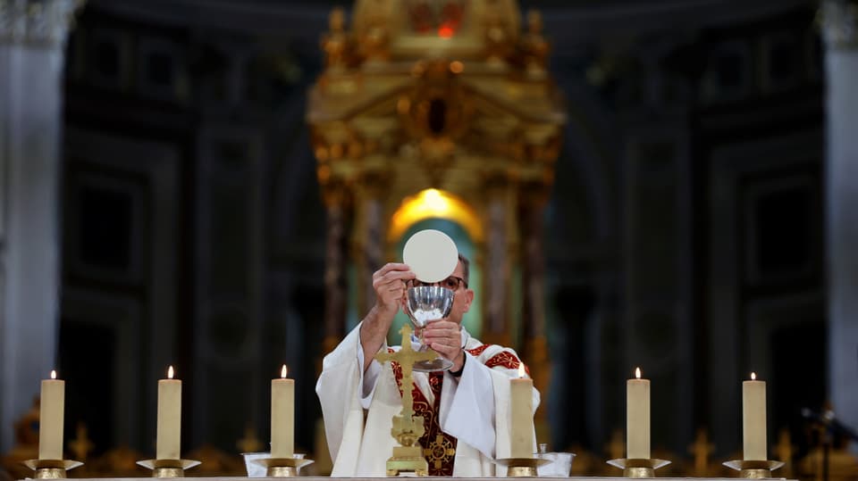 A priest raises the host and a chalice.