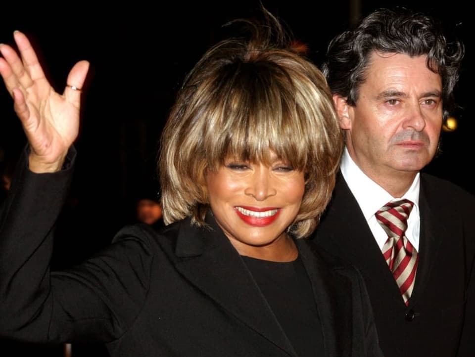 Tina Turner waves at the camera, next to her is her partner Erwin Bach