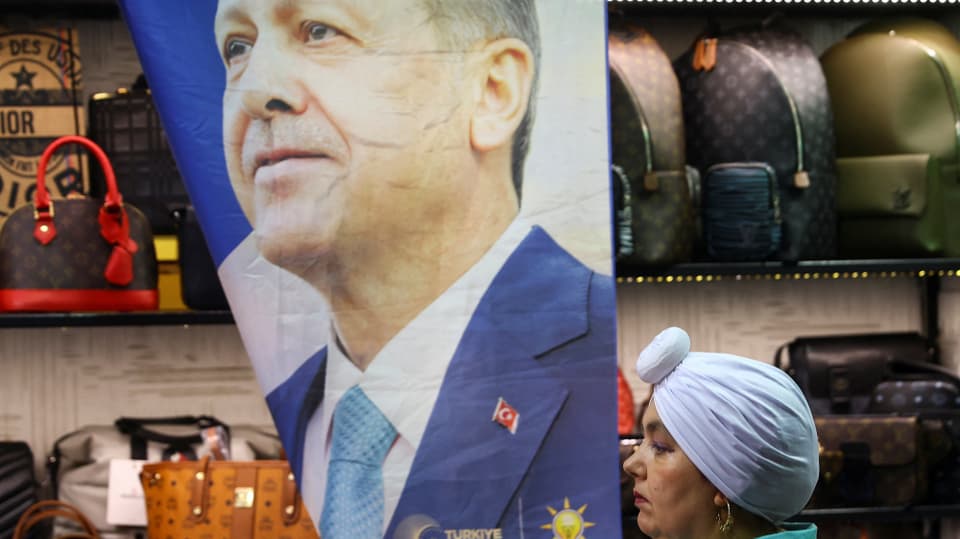 Erdogan looks into the distance on a poster, in front of which a woman is walking past.
