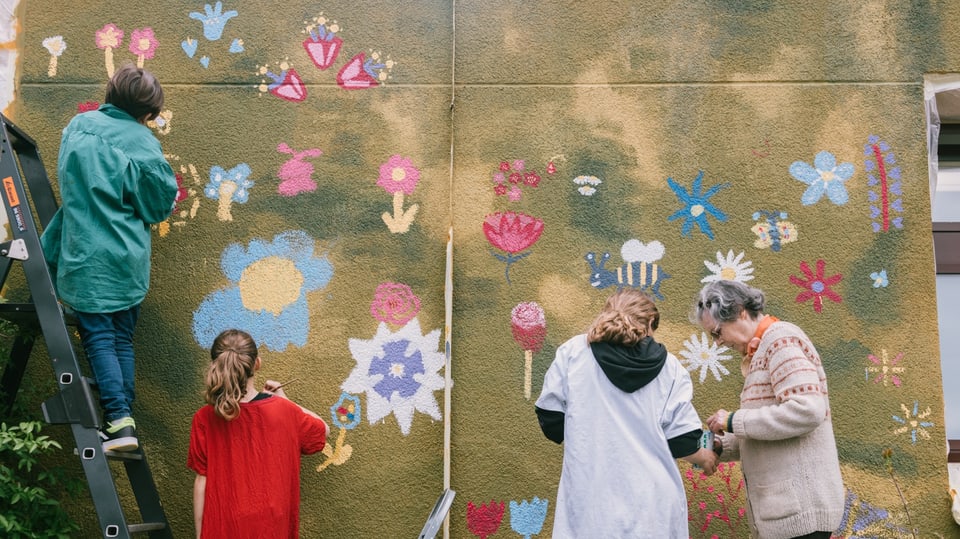 Children, teenagers and a senior paint flowers on a facade.