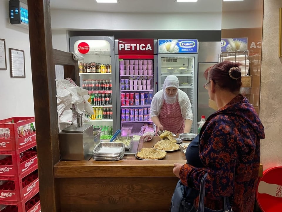 A woman prepares cevapi for a customer.