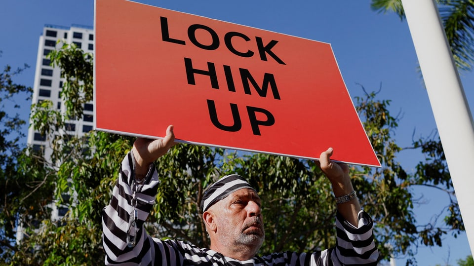 man holding sign.  Lock him up it says.