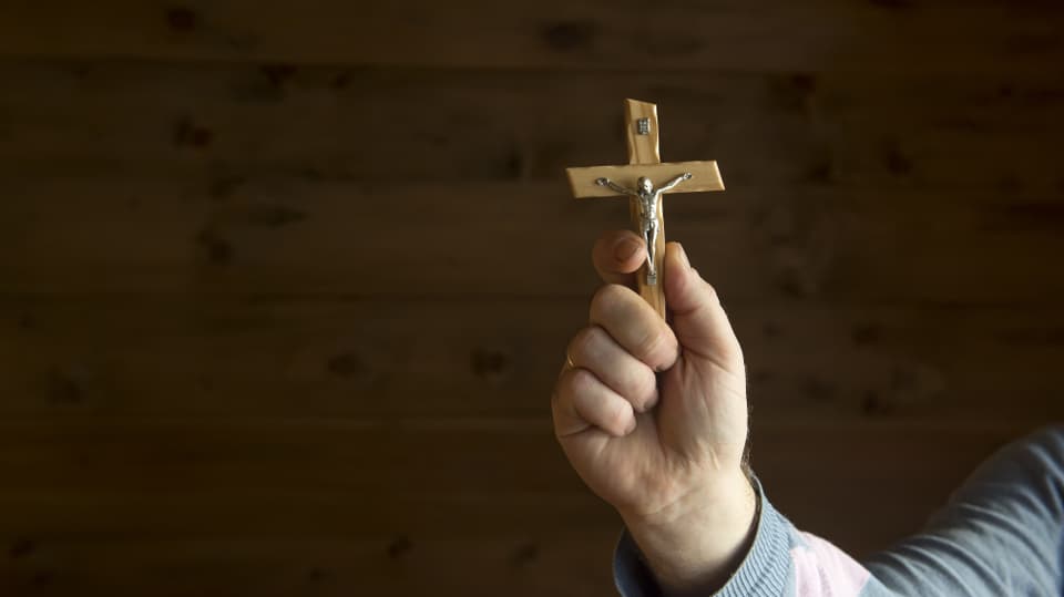 A man's hand holding a crucifix at the camera.