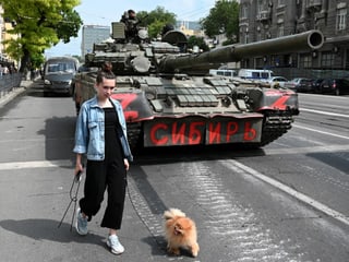 Eine Frau mit einem Hund geht an einem Panzer vorbei, während Kämpfer der privaten Söldnergruppe Wagner in einer Straße in der Nähe des Hauptquartiers des südlichen Militärbezirks in der Stadt Rostow am Don stationiert sind.