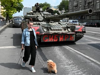 A woman with a dog walks past a tank while fighters from the Wagner private mercenary group are stationed on a street near the headquarters of the Southern Military District in the city of Rostov-on-Don.