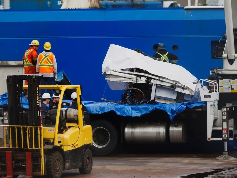 Wreckage is lifted onto a truck with a crane.  The parts are packed.