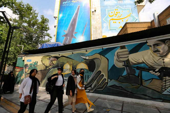 Women walk along a mural behind which appears a giant billboard depicting the 