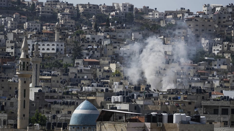A column of white smoke rises between the roofs of Jenin