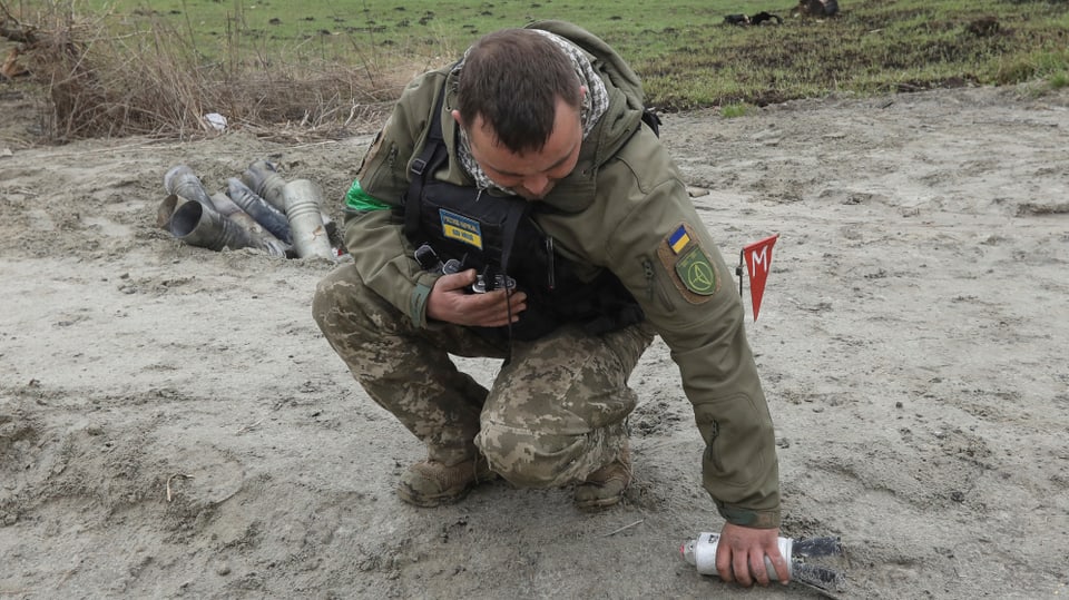 A Ukrainian soldier picks up the case of a cluster bomb after the Russian invasion.