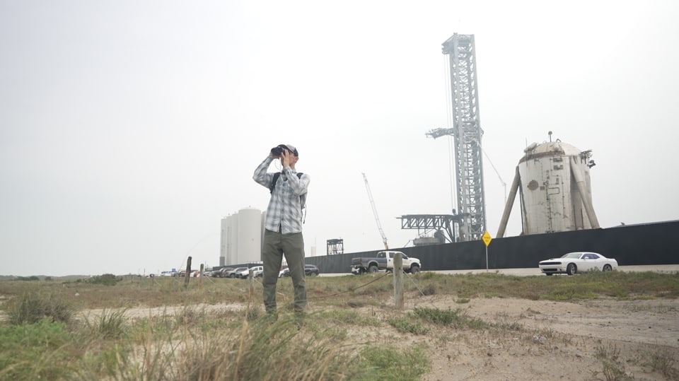 Man in front of SpaceX launch base looks through binoculars