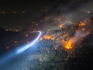 View of lit hillside with blazing flames at night
