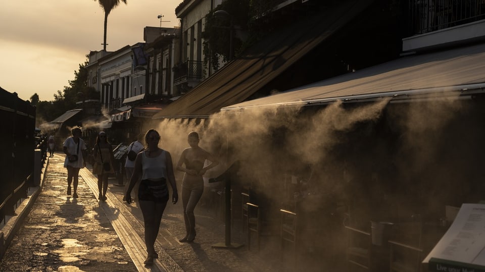 People in Athens' Monastiraki district walk past a fog machine to cool off.
