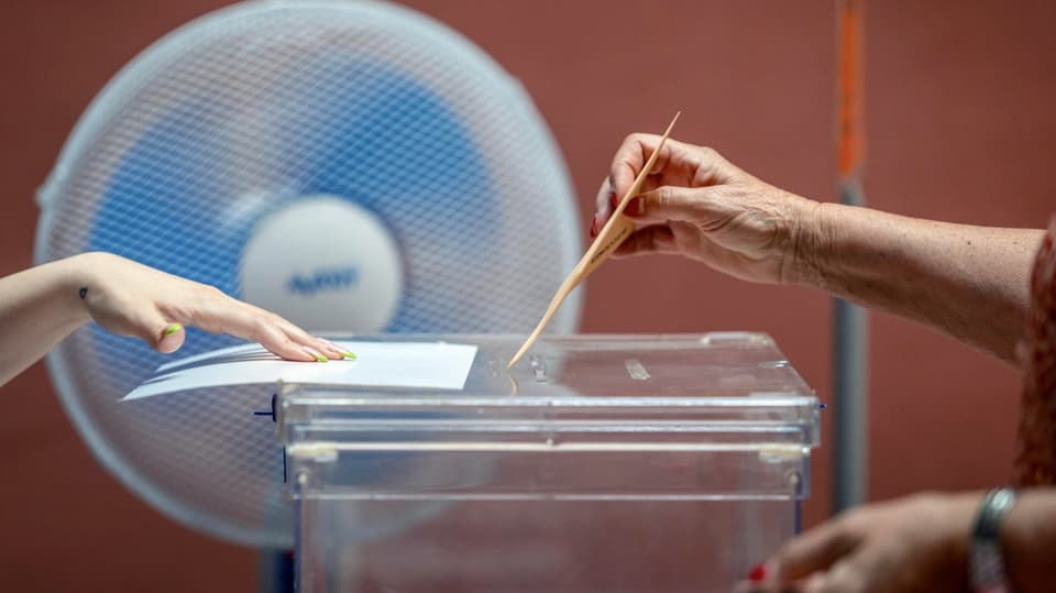 A voter puts his or her ballot paper in the ballot box while a fan hums next to it.