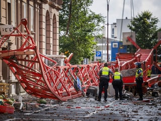 Overturned crane in a street;  next to them are emergency services in fluorescent vests
