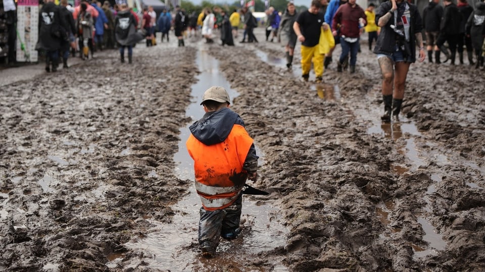 A young boy walks in a tractor mud track filled with water.  Everything around is full of mud.