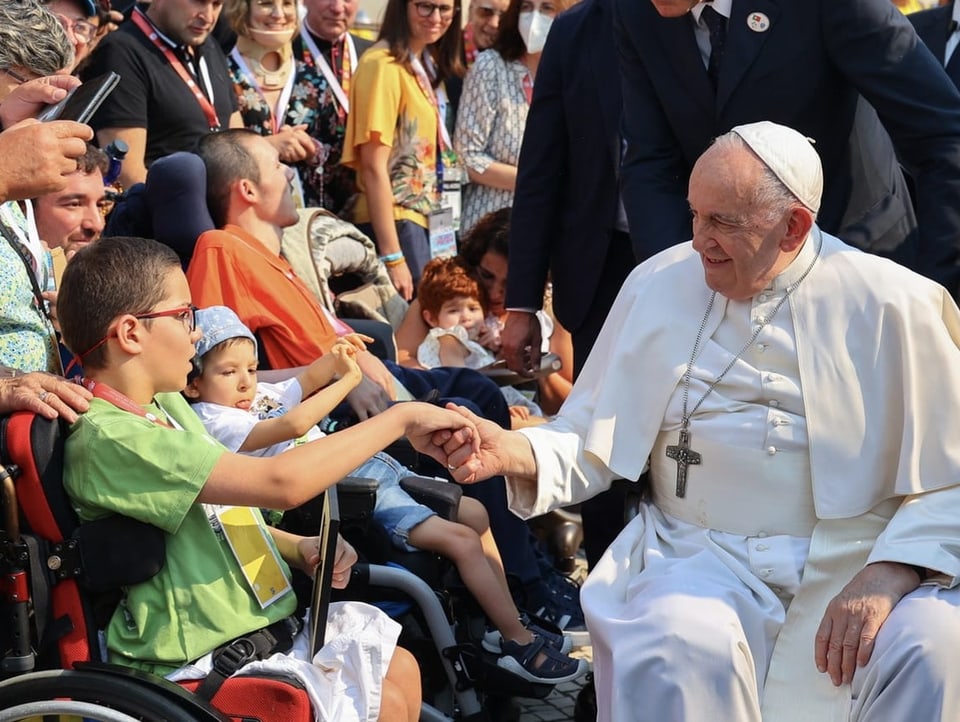 The Pope, himself in a wheelchair, shakes hands with a boy in a wheelchair. 