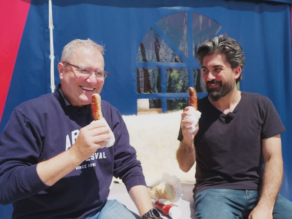 Frank Baumann and Cenk Korkmaz eat a bratwurst together in front of the tent. 