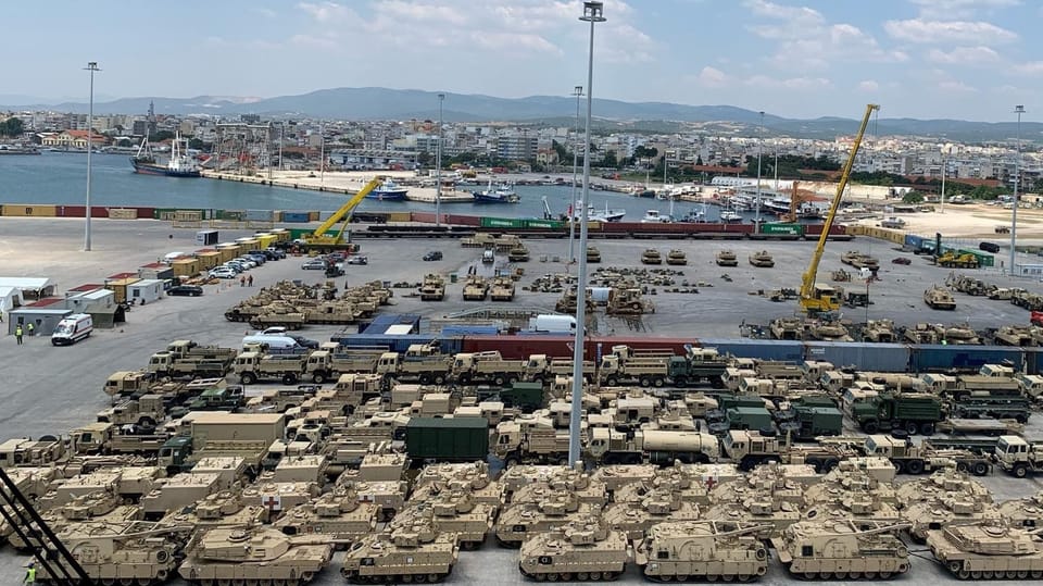 Tanks and military trucks are parked at the harbor docks.