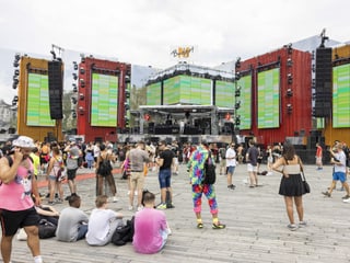 People stand and sit in front of a large stage.  Some are colorfully dressed.