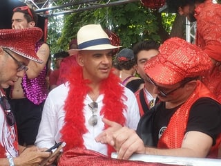 Alain Berset is standing on a Lovemobile.  He wears a red feather boa around his neck.  Someone is talking to him.