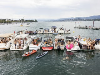 Several boats are lined up in the Zurich lake basin.  People are bustling about on the boats.