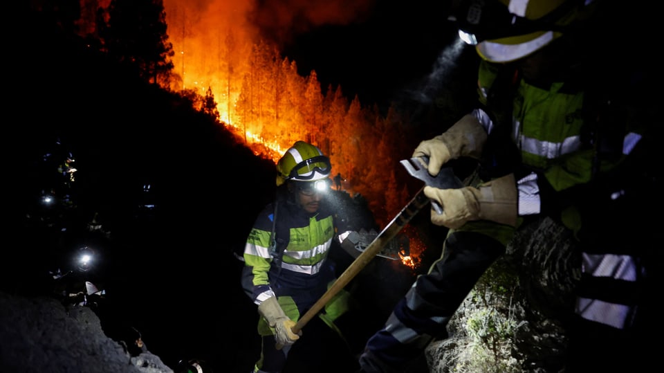Firefighters in front of a forest fire with glowing headlamps.