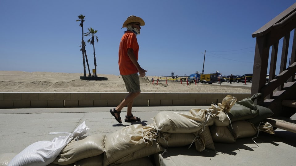 Man walks past sandbags on a beach