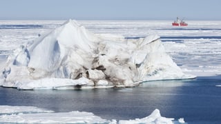 An iceberg lies on the sea in the Arctic.  Behind you can see a freighter. 