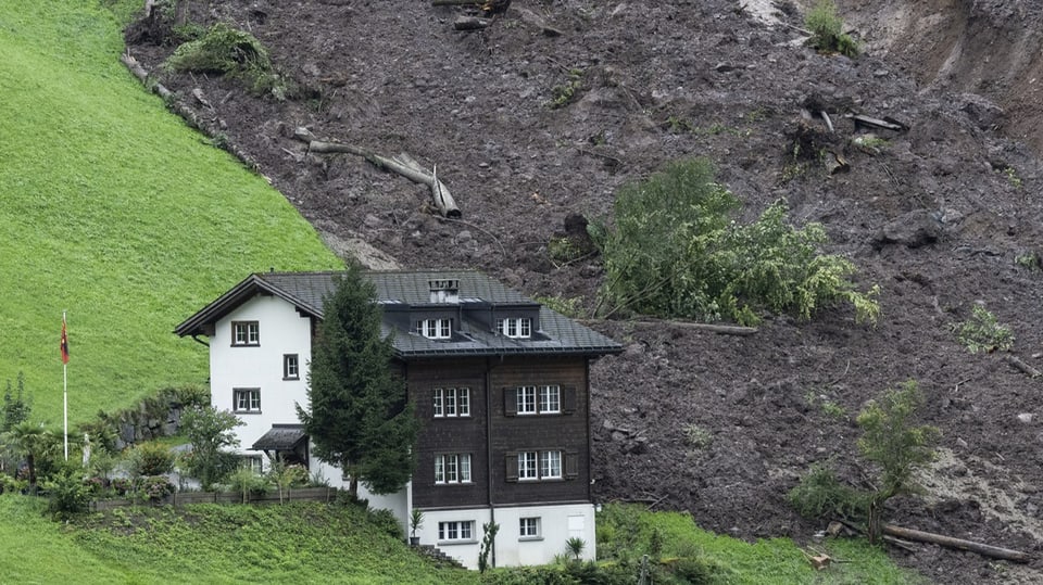View of a mass of rubble right next to a house on a slope in Schwanden