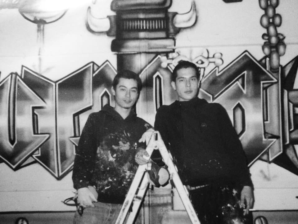 Michi and Tobi Senn on a ladder, with graffiti behind them.