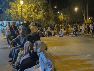 People sit on the street in Morocco after an earthquake at night.