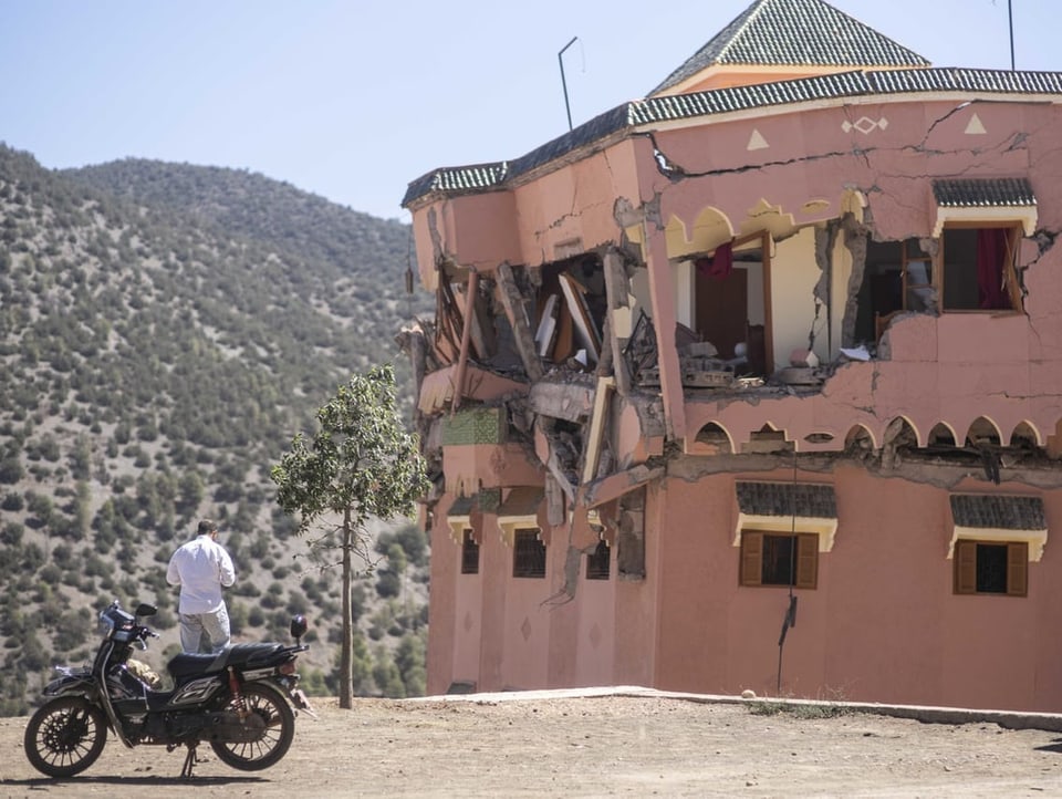 A man stands with a motorcycle next to a destroyed building in Marrakesh.