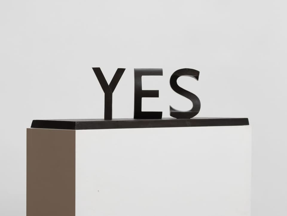 Black lettering sculpture “YES” on a white base, white background