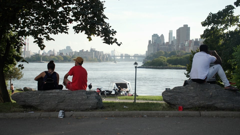 People sitting on rocks, East River and Manhattan in the background.