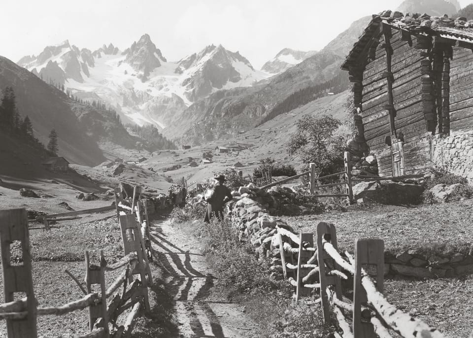 Old photo of a barn with mountain in the background.