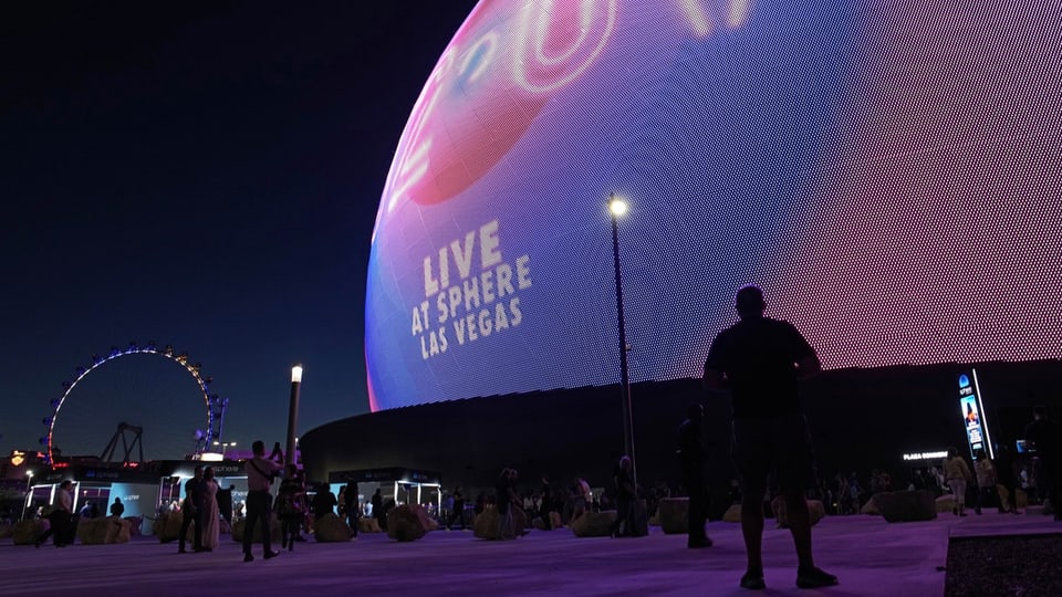 Visitors stand in front of the glowing dome of the Sphere mega event hall.