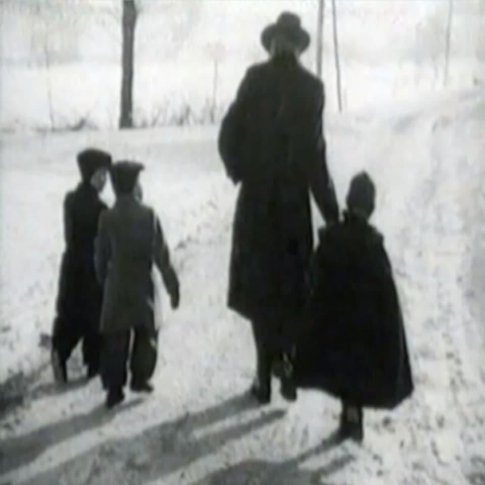 Three children and a man from behind and in winter clothes on a snowy path.  Image is black and white