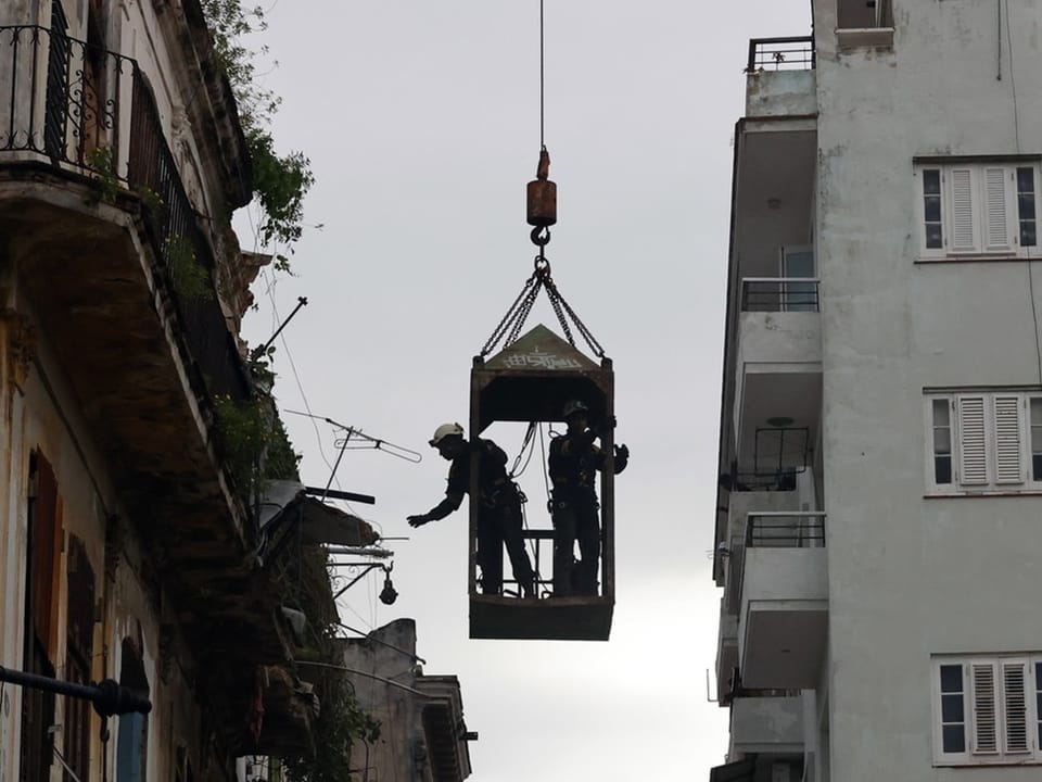 Rescue workers in a capsule being pulled into the air by a crane.