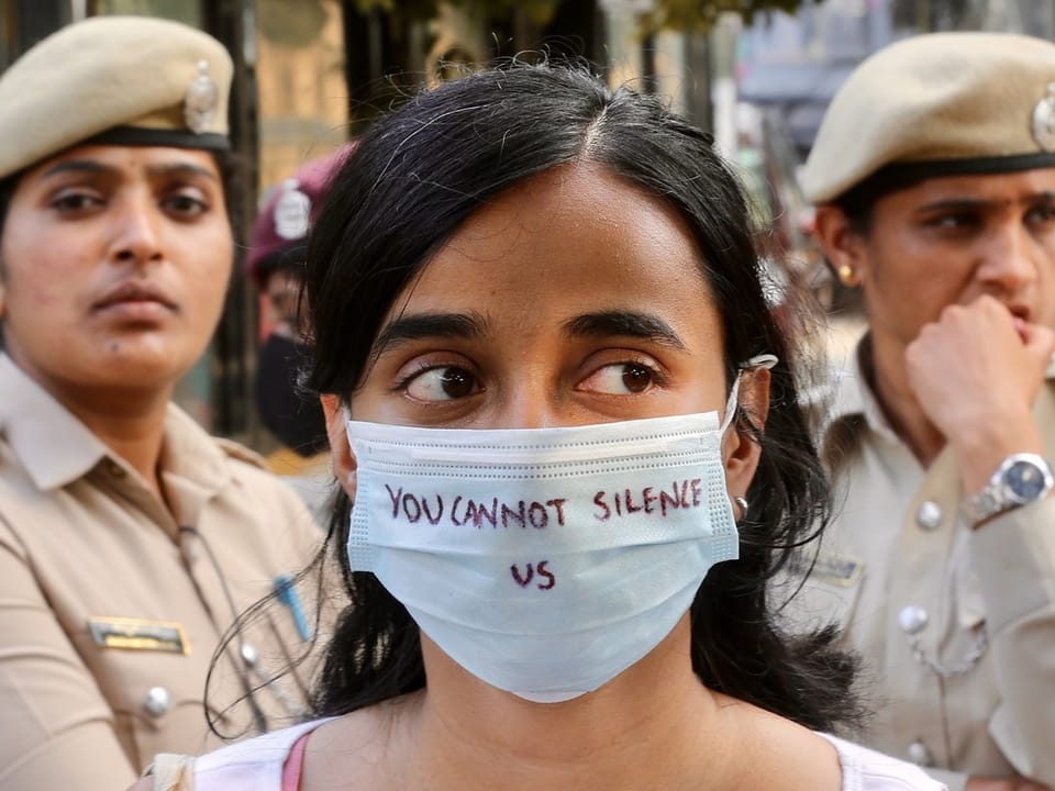 A woman wears a mask with the words “You Can Not Silence Us”