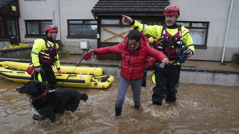 Woman wades through the water with her dog.  She is accompanied by two rescue workers with a rubber boat.