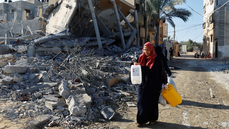 A Palestinian woman walks along a street full of rubble with empty canisters.