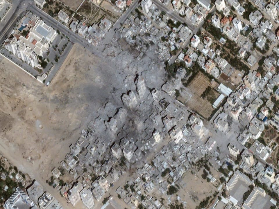 Satellite image of a district of a city.  In the center of the picture there are rubble and partially destroyed buildings.