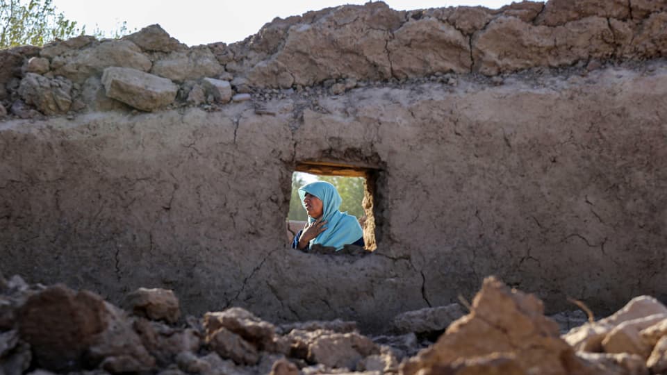View of a crying woman through the small window of a destroyed mud house