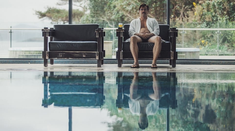 Man in bathrobe and flip-flops sits on one of two designer armchairs by a pool