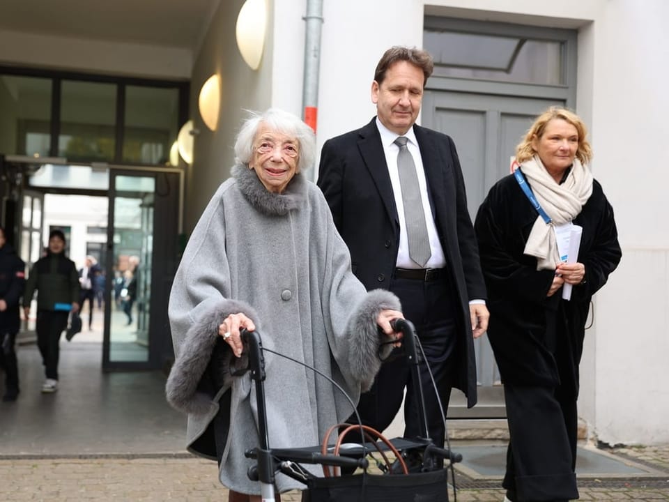 The woman walks, smiling, on a walker next to a man and a woman.